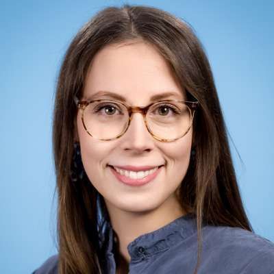 Eine Frau mit Brille und blauem Hemd lächelt in die Kamera.