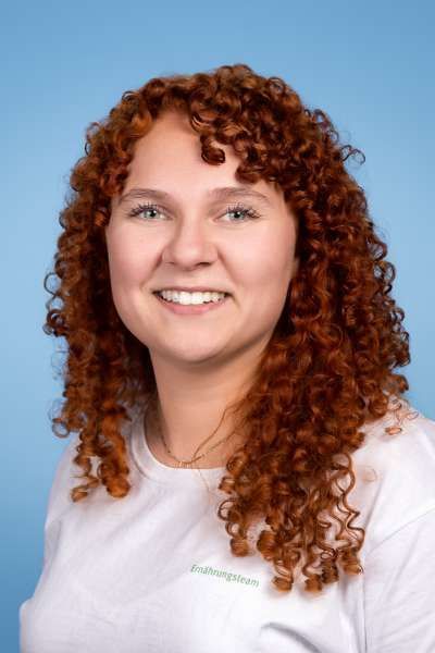 Eine Frau mit roten Locken trägt ein weißes Hemd und lächelt.