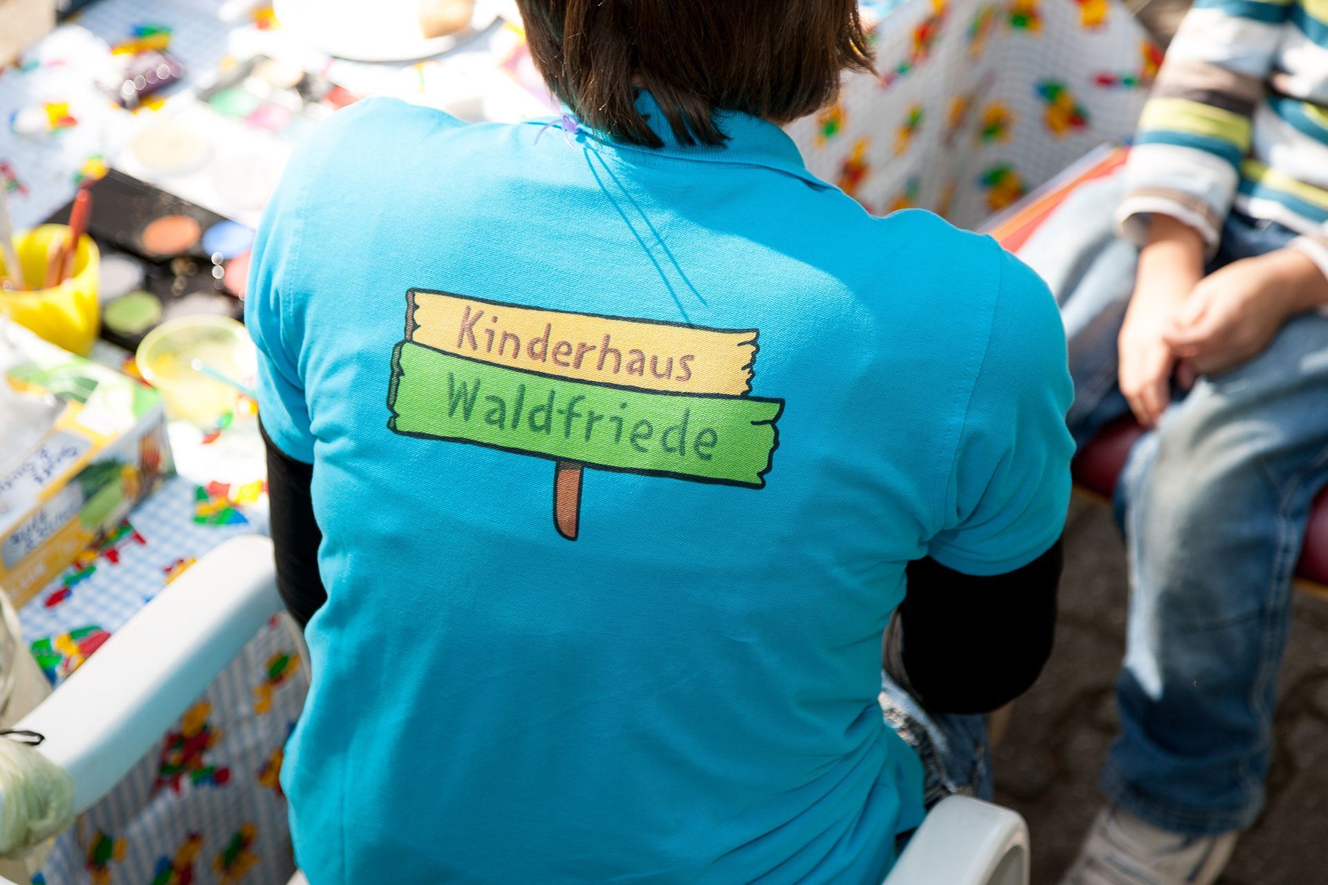 Eine Person, die ein blaues T-Shirt mit der Aufschrift „Kinderhaus Waldfriede“ trägt