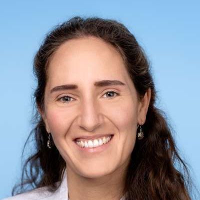 Eine Frau mit langen Haaren und Ohrringen lächelt in die Kamera.