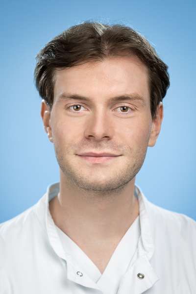 Ein junger Mann im weißen Laborkittel lächelt in die Kamera.