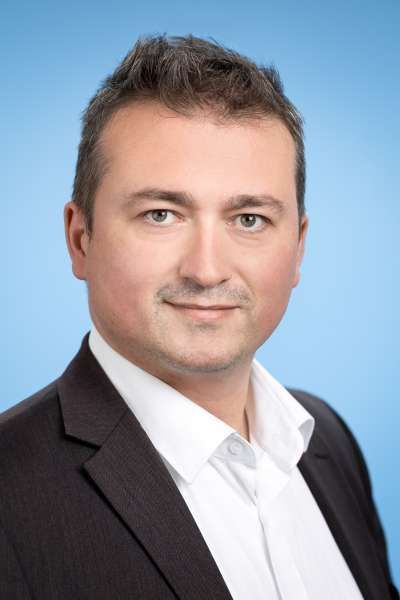 Ein Mann in Anzug und weißem Hemd lächelt in die Kamera.