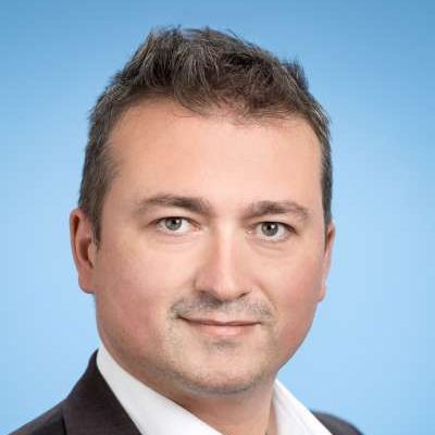 Ein Mann in Anzug und weißem Hemd lächelt in die Kamera.