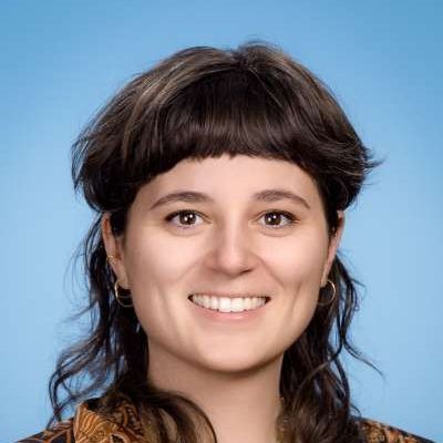 Eine Nahaufnahme des Gesichts einer lächelnden Frau vor blauem Hintergrund.