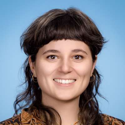 Eine Nahaufnahme des Gesichts einer lächelnden Frau vor blauem Hintergrund.