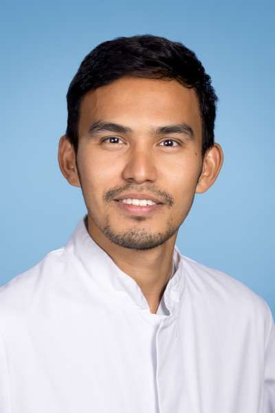 Ein Mann mit Bart trägt ein weißes Hemd und lächelt in die Kamera.