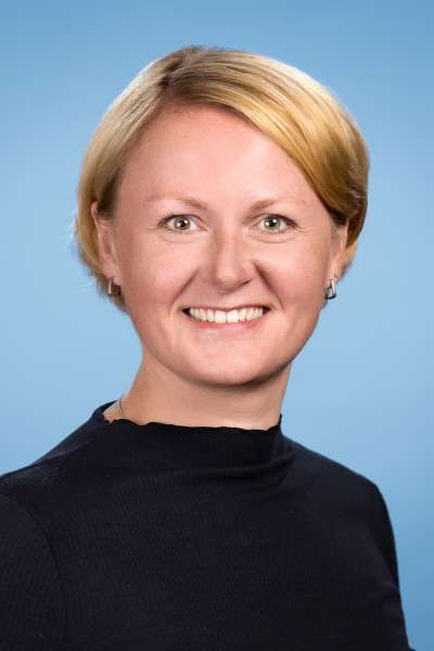 Eine Frau mit blondem Haar trägt ein schwarzes Hemd und lächelt in die Kamera.