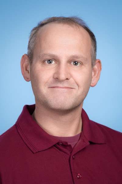 Ein Mann in einem roten Hemd lächelt in die Kamera.