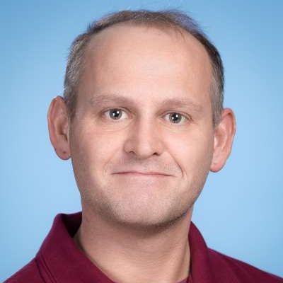 Ein Mann in einem roten Hemd lächelt in die Kamera.