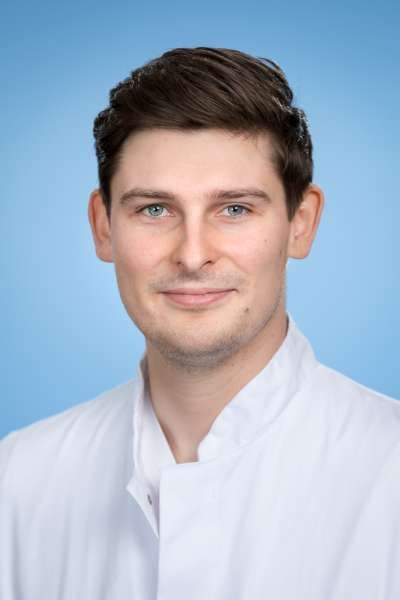 Ein Mann im weißen Laborkittel lächelt in die Kamera.