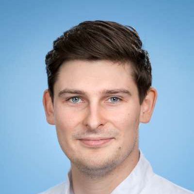 Eine Nahaufnahme des Gesichts eines Mannes vor blauem Hintergrund.