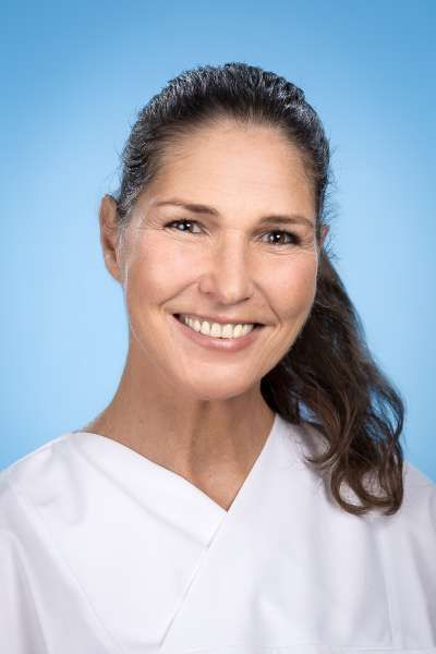 Eine Frau in einem weißen Kasack lächelt in die Kamera.