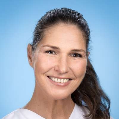 Eine Frau im weißen Kittel lächelt in die Kamera.