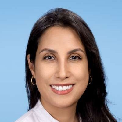 Eine Frau in einem weißen Hemd und mit Ohrringen lächelt in die Kamera.