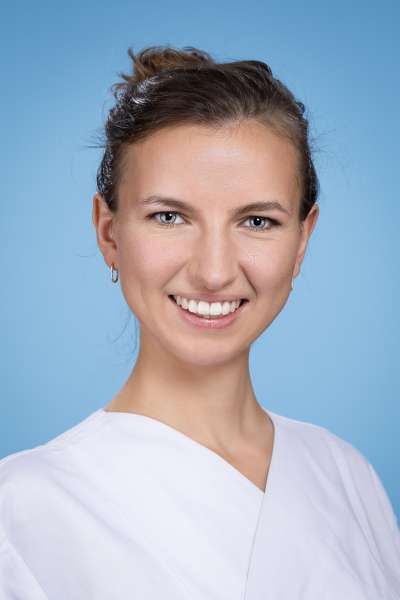 Eine Frau im weißen Kittel lächelt in die Kamera.