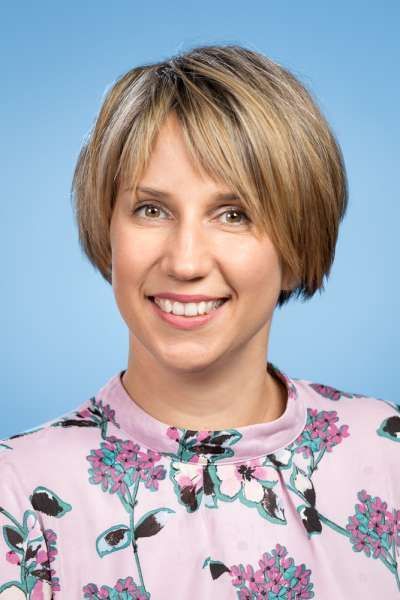 Eine Frau in einem rosa Hemd mit Blumenmuster lächelt in die Kamera.