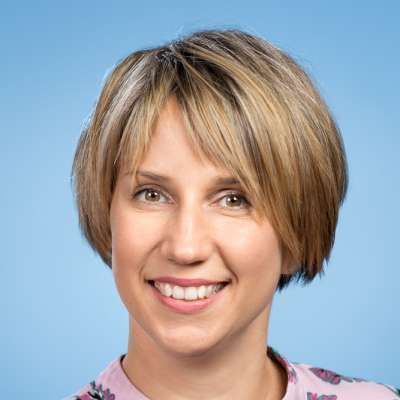 Eine Frau mit kurzen blonden Haaren lächelt und trägt ein rosa Hemd.