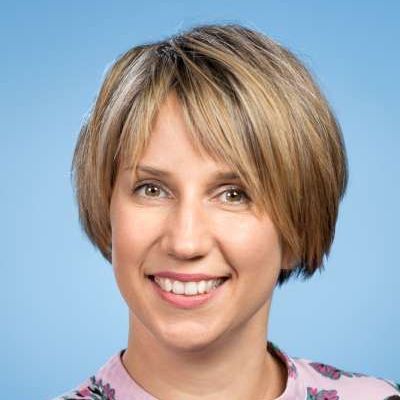 Eine Frau mit kurzen blonden Haaren lächelt und trägt ein rosa Hemd.