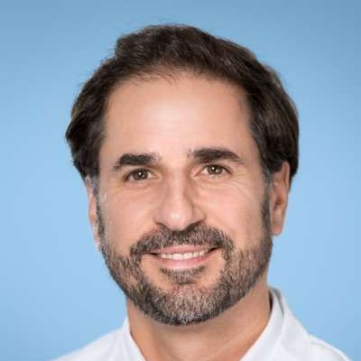 Ein Mann mit Bart und einem weißen Hemd lächelt in die Kamera.