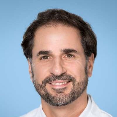 Ein Mann mit Bart und einem weißen Hemd lächelt in die Kamera.