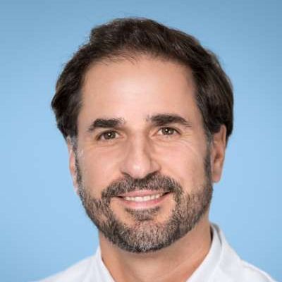 Ein Mann mit Bart und einem weißen Hemd lächelt in die Kamera.