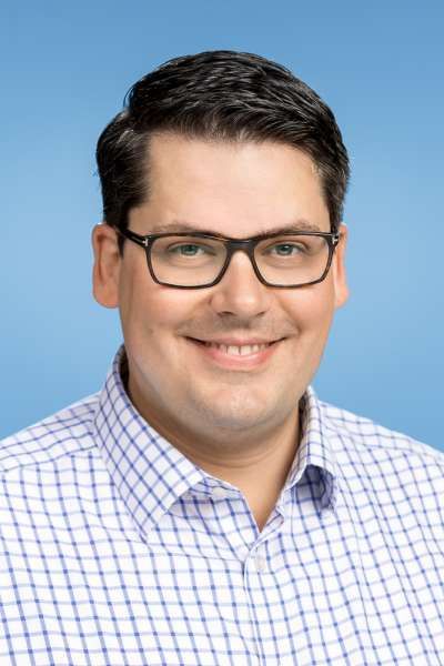 Ein Mann mit Brille und kariertem Hemd lächelt in die Kamera.