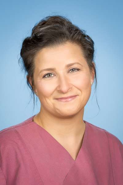 Eine Frau in einem rosa OP-Kittel lächelt in die Kamera.