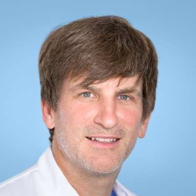 Ein Mann mit braunem Haar und Bart lächelt in die Kamera.