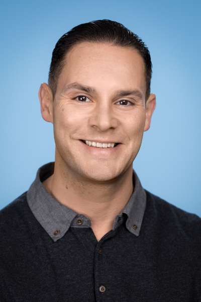 Vor einem blauen Hintergrund lächelt ein Mann in die Kamera.