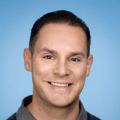 Ein Mann in einem grauen Hemd lächelt in die Kamera.