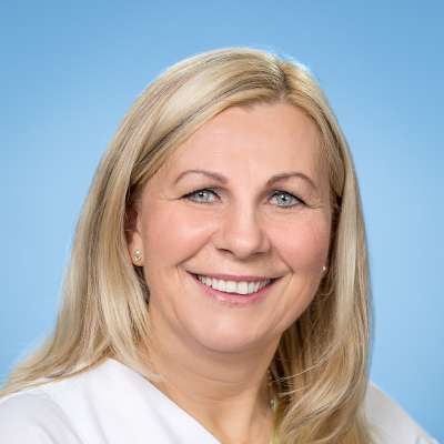 Eine Frau im weißen Kittel lächelt in die Kamera.