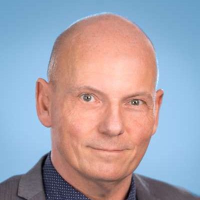 Ein kahlköpfiger Mann in Anzug und Krawatte lächelt in die Kamera.