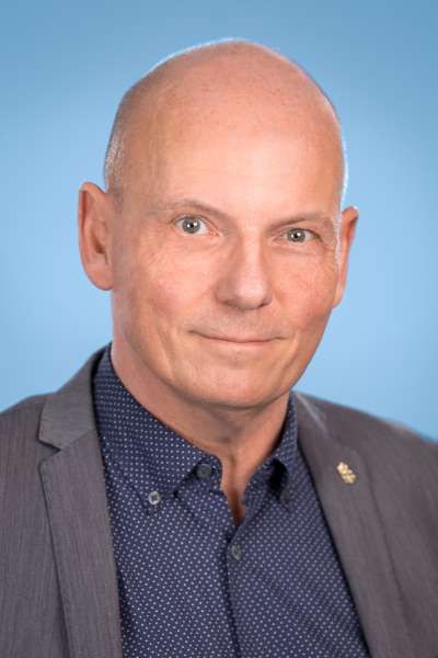 Ein kahlköpfiger Mann in Anzug und blauem Hemd lächelt in die Kamera.