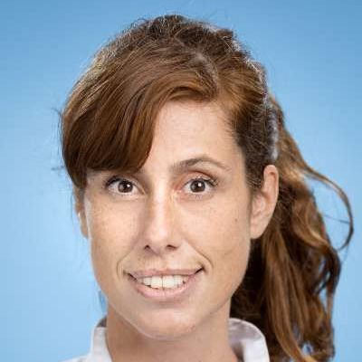 Eine Frau mit braunem Haar lächelt und trägt ein weißes Hemd.