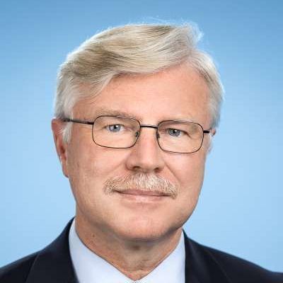 Eine Frau in einem schwarzen Pullover und einem weißen Hemd lächelt in die Kamera.