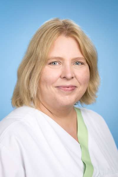 Eine Frau im weißen Kittel lächelt in die Kamera.