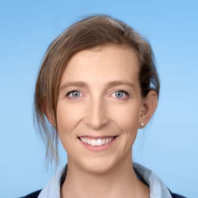 Vor einem blauen Hintergrund lächelt eine Frau in die Kamera.