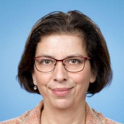 Eine Frau mit Brille und Ohrringen lächelt in die Kamera.