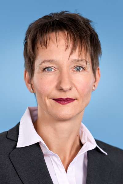 Eine Frau in Anzug und weißem Hemd lächelt in die Kamera.