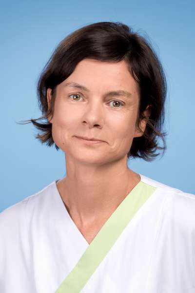 Eine Frau trägt einen weißen Kasack mit einer grünen Schleife um den Hals.