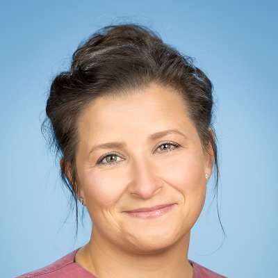 Eine Frau lächelt in die Kamera und trägt ein rosa Hemd.