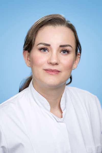 Eine Frau in einem weißen Laborkittel steht vor einem blauen Hintergrund.