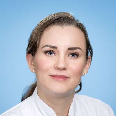 Eine Frau in einem weißen Hemd schaut vor einem blauen Hintergrund in die Kamera.