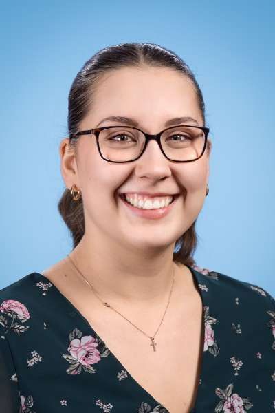 Eine Frau mit Brille und geblümtem Hemd lächelt in die Kamera.