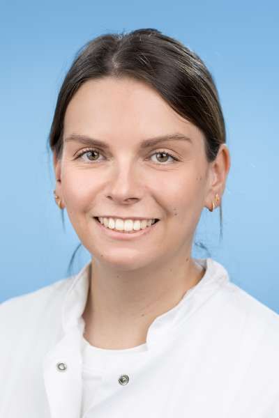 Eine Frau im weißen Kittel lächelt in die Kamera.