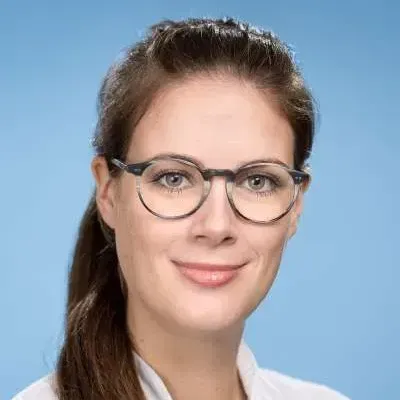 Eine Frau mit Brille und weißem Hemd lächelt in die Kamera.