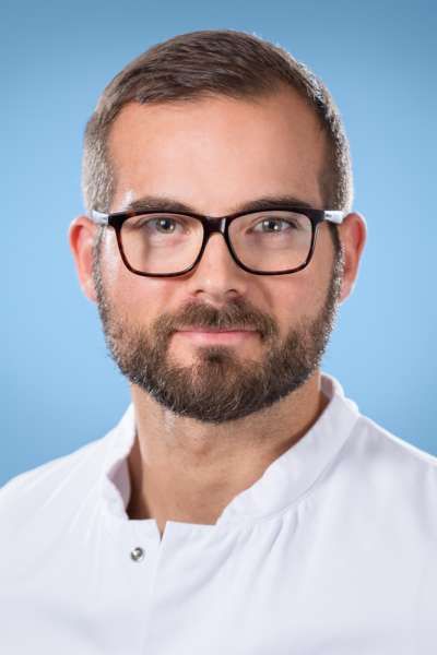 Ein Mann mit Bart und Brille trägt einen weißen Laborkittel.