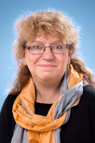 Eine Frau mit Brille und Schal lächelt in die Kamera.