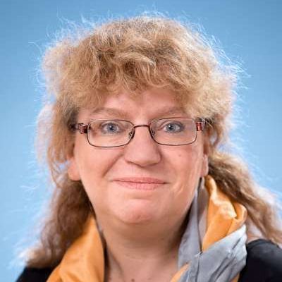 Eine Frau mit Brille und Schal lächelt in die Kamera.