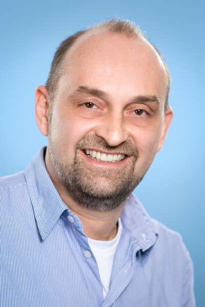 Ein Mann mit Bart und blauem Hemd lächelt in die Kamera.